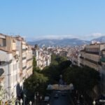 View down a Marseille street past rooftops and a large wall mural toward distant hills.