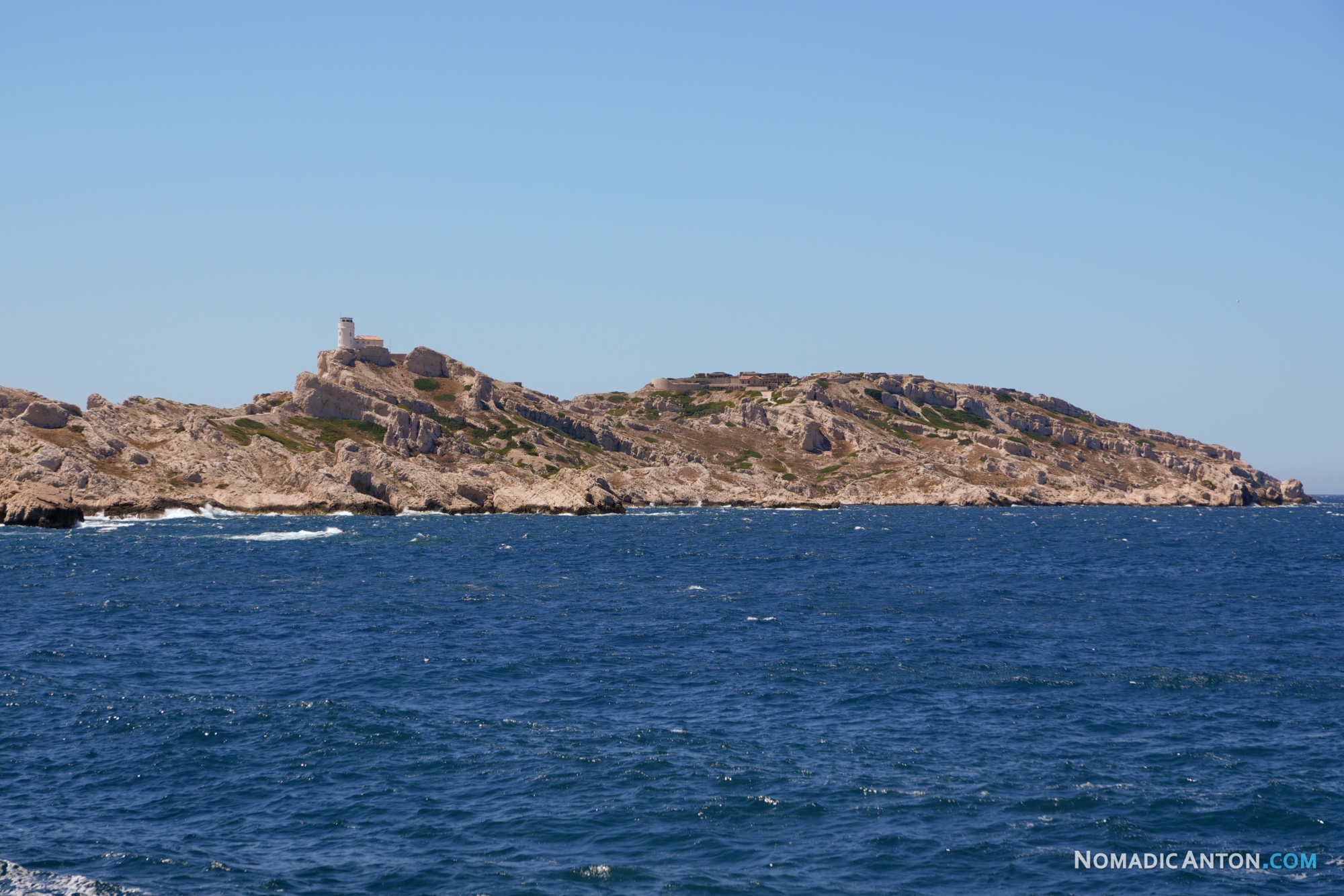 Rocky island with a small stone tower above choppy blue water.