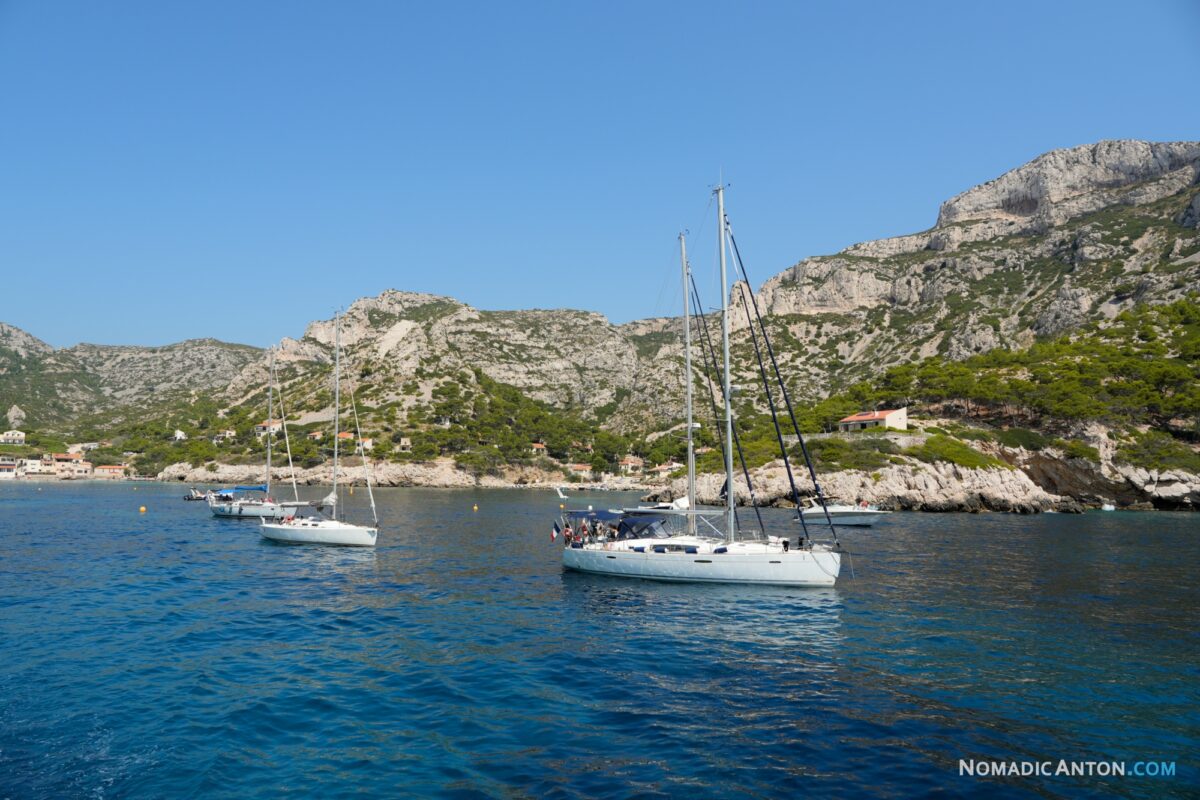 Sailboats on blue water beside the rocky slopes of a calanque.