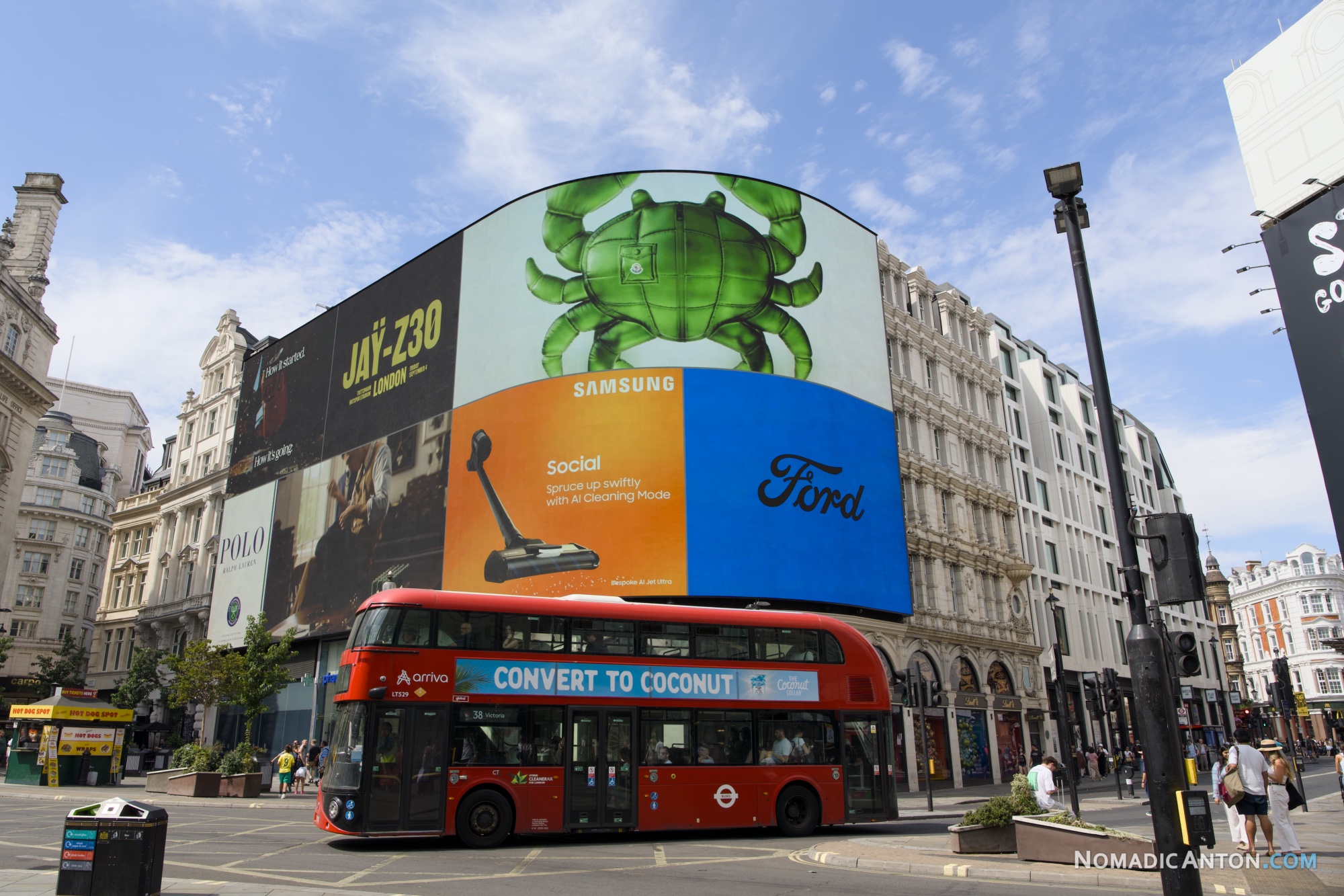 Red double-decker bus passing under the digital billboards at Piccadilly Circus